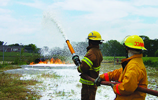 两个消防科学专业的学生拿着水管指着火场