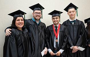 四名毕业生戴着帽子，穿着长袍，微笑着